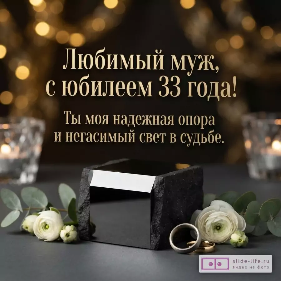 Темный фон с золотистыми огнями боке, внизу черная глянцевая подставка, белые цветы и два обручальных кольца. Текст: «Любимый муж, с юбилеем 33 года! Ты моя надежная опора и негасимый свет в судьбе.»