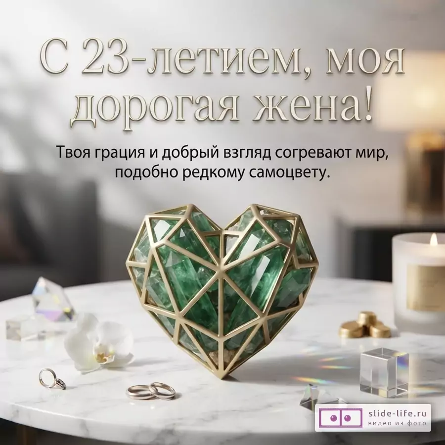 Зеленый кристалл в форме сердца в золотом каркасе на мраморном столе рядом с кольцами, свечой и текстом «С 23-летием, моя дорогая жена! Твоя грация и добрый взгляд согревают мир...».